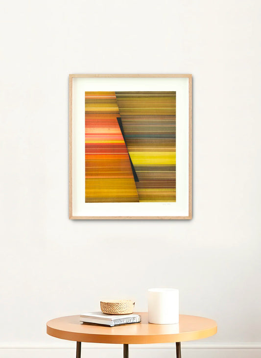 Framed abstract art piece on a white wall above a wooden table with decor items.