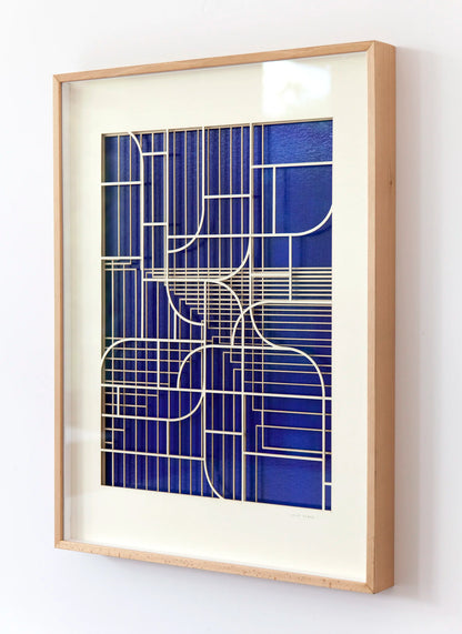 Oblique angled view of geometric abstract artwork by Jesús Perea, showing the overlapping laser-cut museum board layers that create a three-dimensional relief over the blue background.